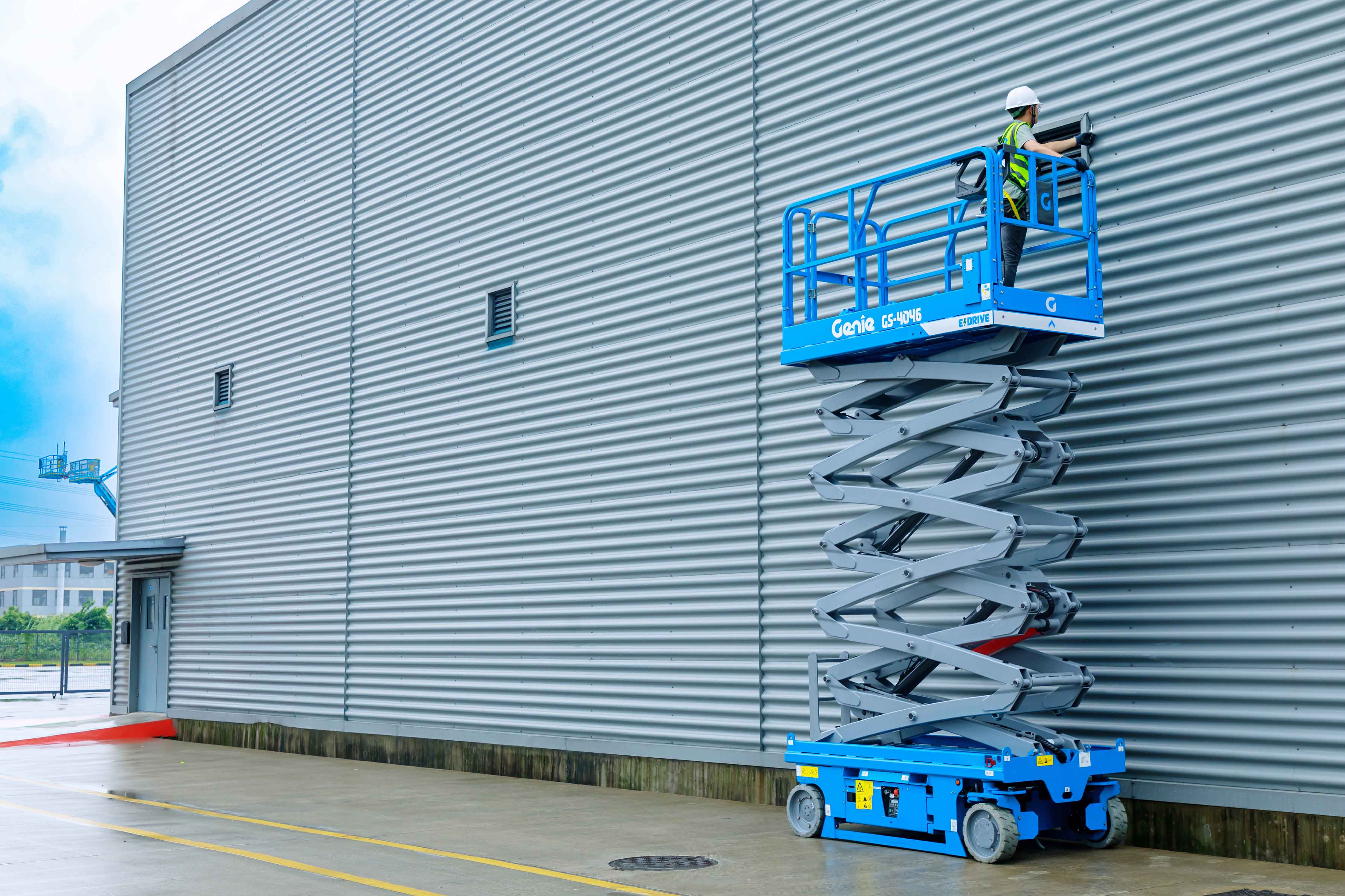 A glazier installs a pane of glass on the exterior of a building while standing on a Genie scissor lift work platform that’s elevated several feet in the air.